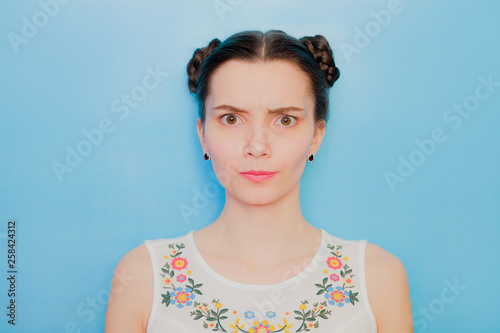 Funny cute girl on a blue studio background. Bright emotional female portrait. Angry soft face