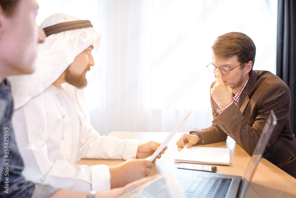 Fototapeta premium Arabian businessman signing cooperation agreement in office, another businessman submit documents. Arab business concept 