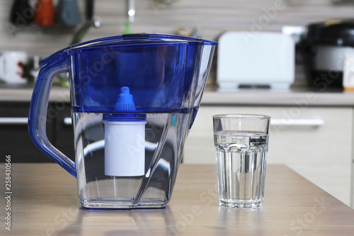 Glass of clean water and filter for cleaning drinking water on the table in the kitchen. Purification of drinking water at home.