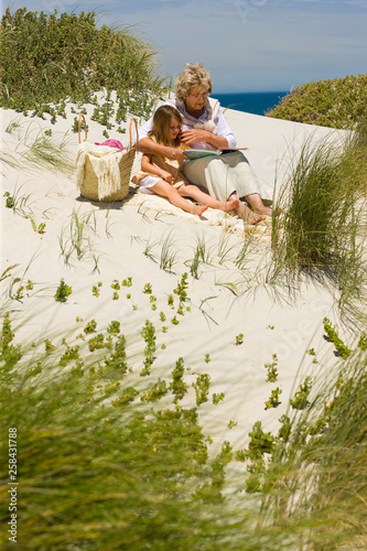Grand mother and grand daughter reading on the beach