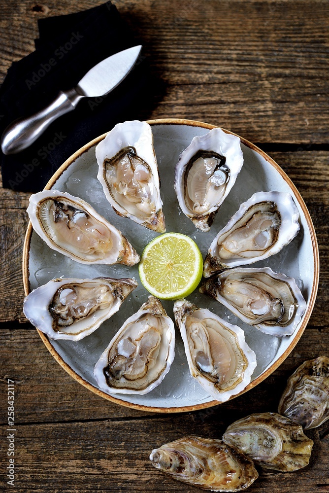 Fresh ocean oysters with slices of lemon on ice on old wooden background. Top view. Fresh ocean oysters with slices of lemon on ice on old wooden background. Top view.