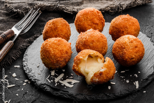 Fried potato cheese balls or croquettes with spices on black plate over dark stone background. Unhealthy food