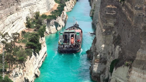 CORINTH, GREECE - CIRCA MAY 2018: Among the rocks in turquoise water floating a Cargo ship. Beautiful scenery of the Corinth Canal in a bright sunny day