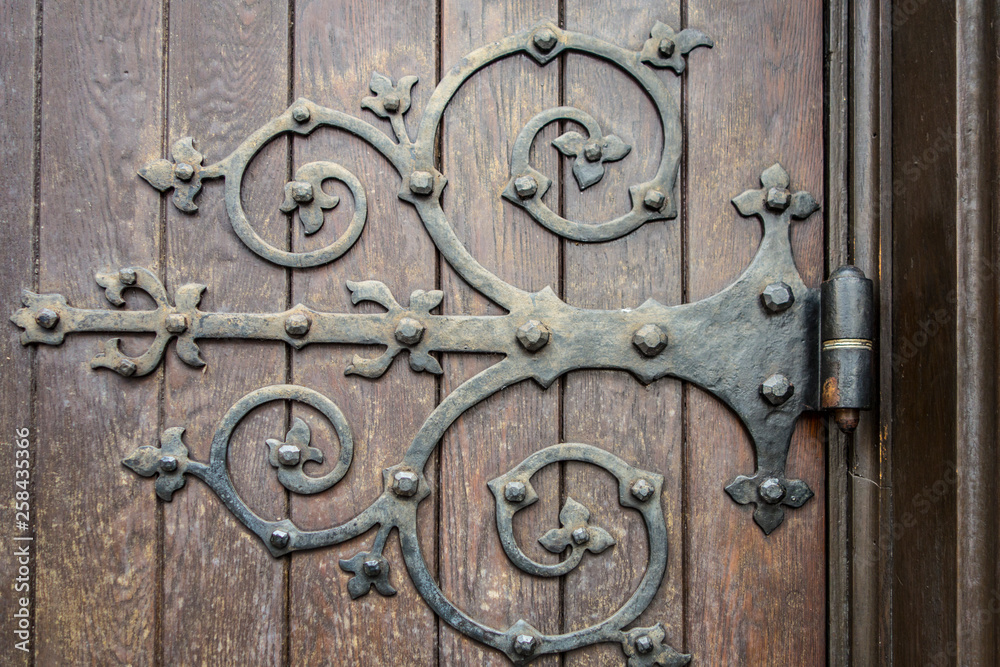 close up of big ornate cast iron door hinge on wood plank door close up of big ornate cast iron door hinge on wood plank door