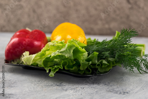 Ingredients for vegetarian dishes. Yellow and red sweet pepper, leaves of fresh lettuce and dill. Black glass plate on a light background.