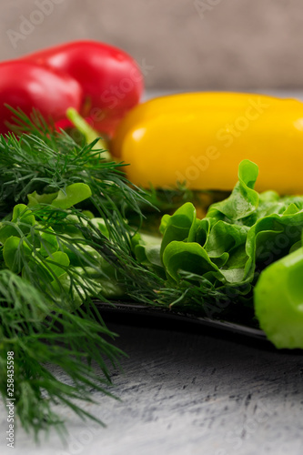 Green salad leaves, fresh dill for cooking vegetarian dishes with red and yellow peppers. Vertical, close-up.