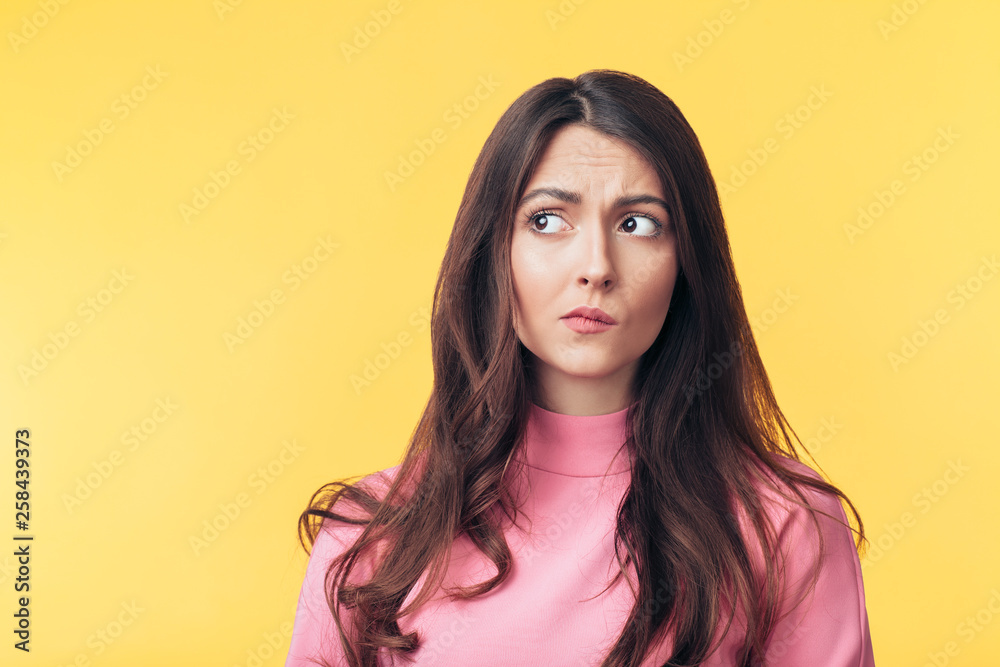Thoughtful confused woman looking away isolated over yellow background Thoughtful confused woman looking away isolated over yellow background