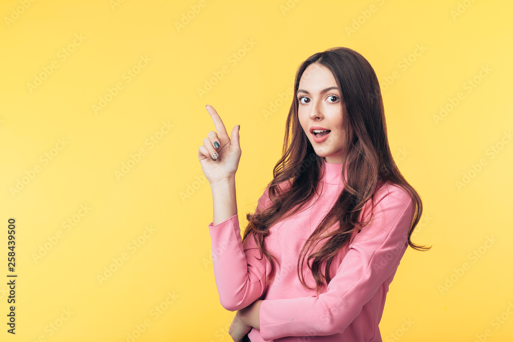 Beautiful surprised woman showing empty copy space pointing her fingers isolated on yellow background