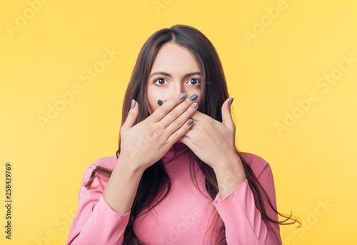 Surprised excited woman covering her mouth with hands on yellow background photo