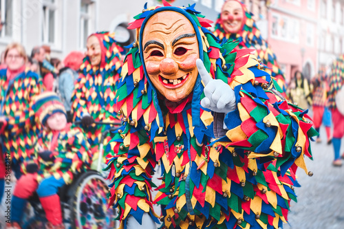 Colorful carnival figure with pretty wooden mask shows a gesture with the index finger. Street Carnival in Southern Germany - Black Forest.