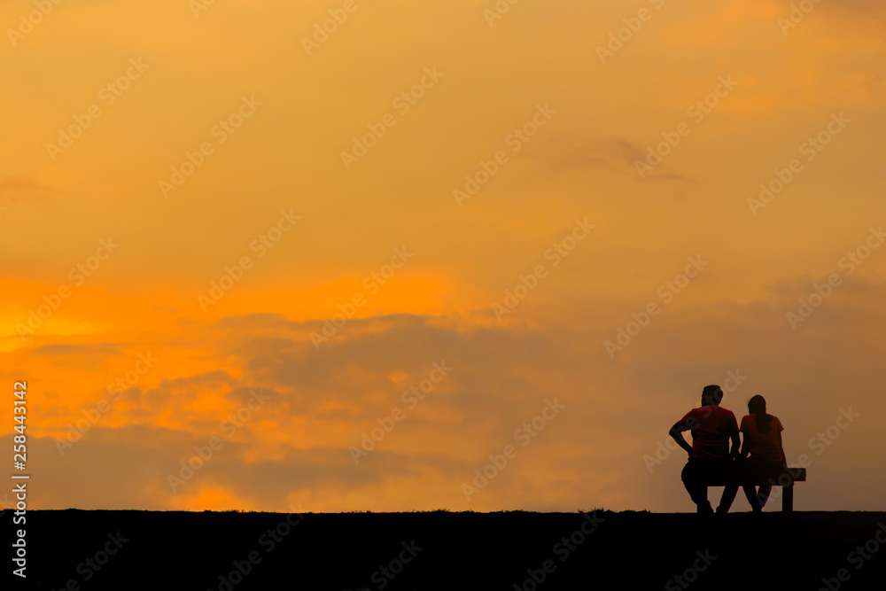 Back view of a couple silhouette sitting on Chair at colorful sunset on background Back view of a couple silhouette sitting on Chair at colorful sunset on background