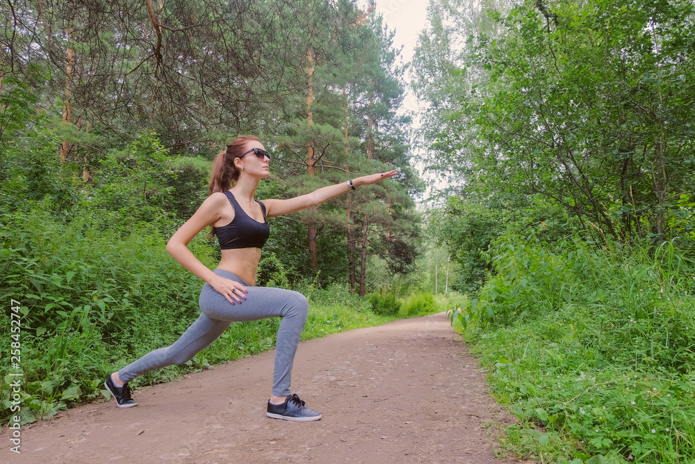 Athletic slim girl doing lunges in the woods. Training in nature.