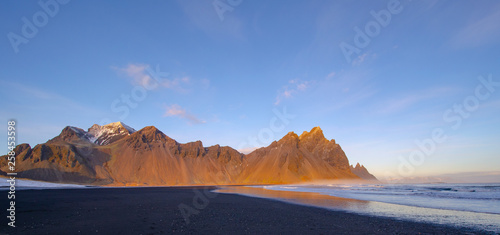 Golden Mountain on black sand beach in Iceland, with ice, snow, and golden light