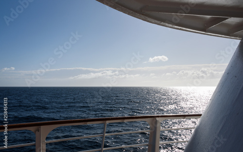 View of blue sky and blue ocean with sun low on horizon from outside deck of cruise ship, Atlantic Ocean