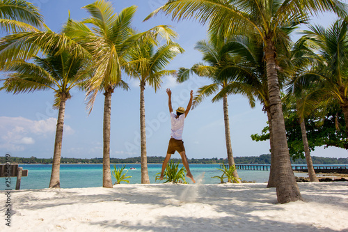 young man is jumping on the white beach with palm trees during happy time on vacation in Koh Kham  Trat  Thailand.