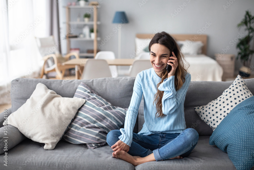 Attractive smiling woman talking on the phone while sitting on the sofa.