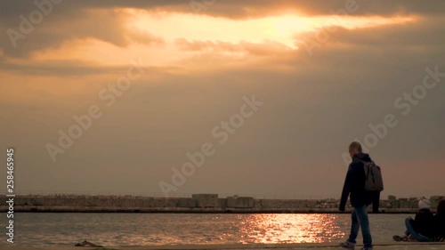 Thessaloniki / Greece 28 march 2019 :A man is walking to the sea shore some girls are  seating  in the road by the sea but they are leaving they all enjoy the good weather and the sunset