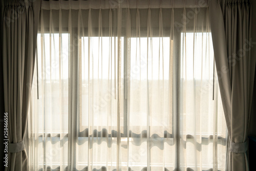 Morning sunlight shining through the transparent curtain on window shade in empty bedroom.