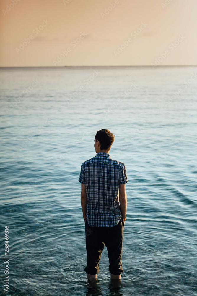 A young guy on the seashore at sunrise and looks into the distance A young guy on the seashore at sunrise and looks into the distance
