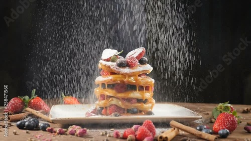 Chef Sprinkling sugar powder on tasty pancake, slow motion. Flour being sieved onto pancakes. Close-up pancakes stack on plate being decorated with cranberries and dusted with powdered sugar