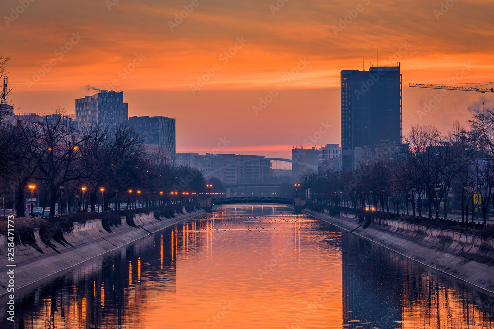 Vibrant cityscape shot early morning before sunrise in Bucharest with a river in the foreground with ducks swimming
