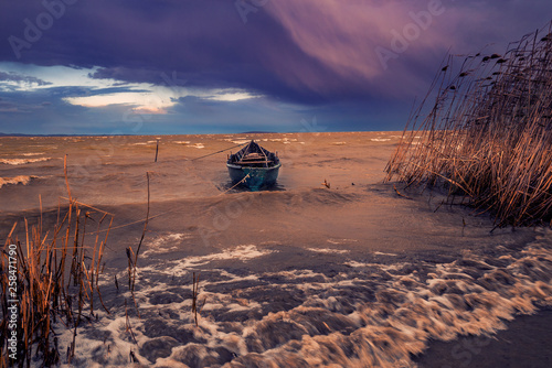 Fishing boat on a lake on a windy day during a storm tied up to the shore against dramatic clouds and big waves