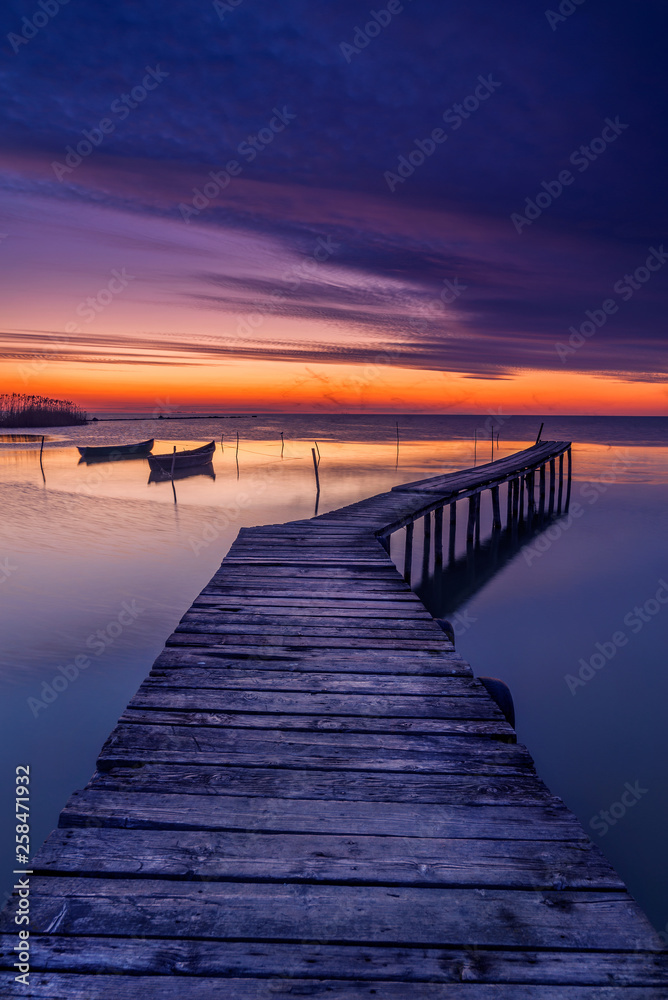 Pontoon used by the fishermen to get to their boats captured before sunrise with two fishing boats in the background and shadows of flying birds due to long exposure