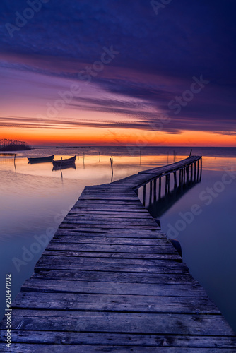 Pontoon used by the fishermen to get to their boats captured before sunrise with two fishing boats in the background and shadows of flying birds due to long exposure © ionutpetrea