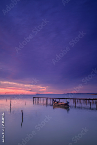 Motorized fishing boat near a pontoon captured before sunrise with  shadows of flying birds due to long exposure