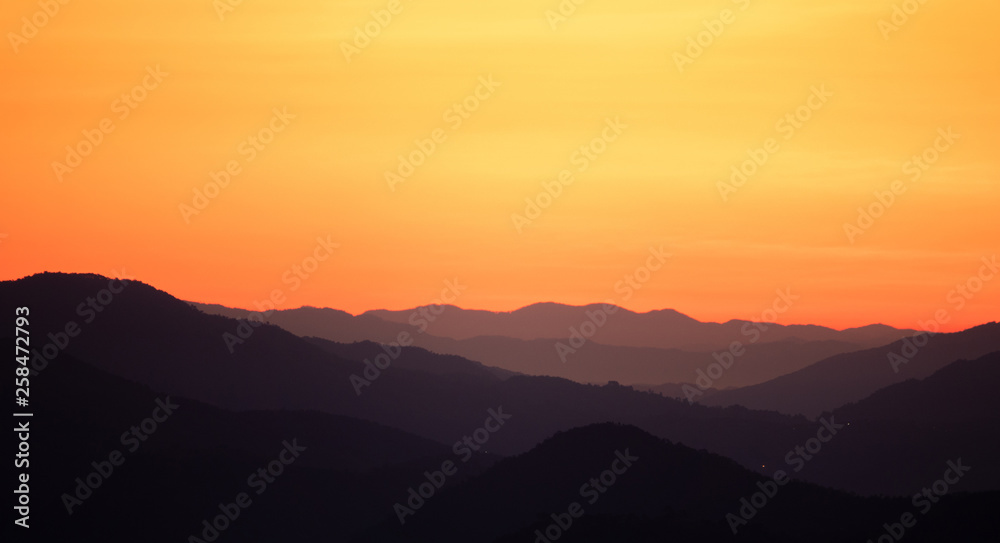 Landscape view black mountains and forest silhouette under skyscape orange gradients morning sunlight with mist and fog. Northern in Thailand.