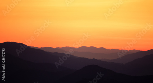Fototapeta Naklejka Na Ścianę i Meble -  Landscape view black mountains and forest silhouette under skyscape orange gradients morning sunlight with mist and fog. Northern in Thailand.