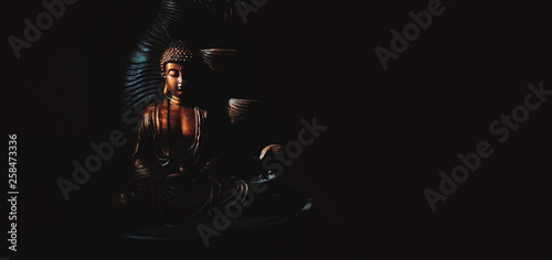 Golden Gautama Buddha statue with a black background depicting darkness and hope coming in form of sunlight.