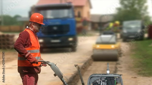 Construction worker operating a vibratory plate compactor on a road work site.