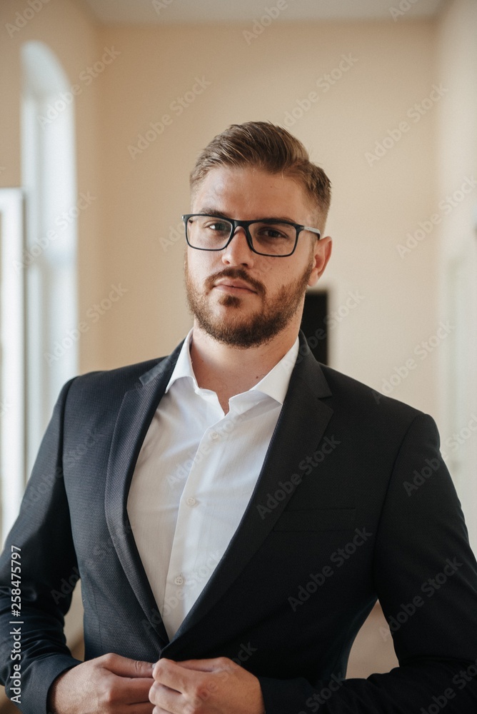 A man in a black suit and white shirt poses indoors for advertising men's clothing. Shooting for men's clothing store A man in a black suit and white shirt poses indoors for advertising men's clothing. Shooting for men's clothing store
