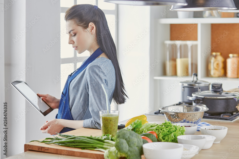 Happy woman looking recipe tablet kitchen reading cooking Happy woman looking recipe tablet kitchen reading cooking