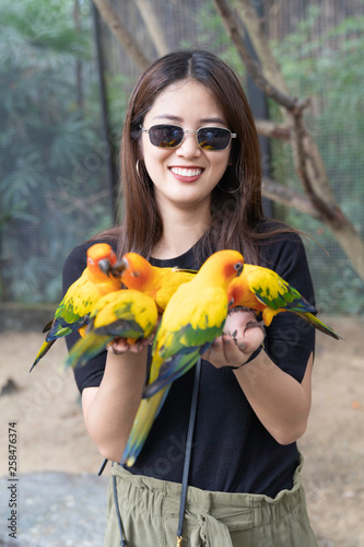 Asian beautiful woman enjoying with love bird on hand and body.