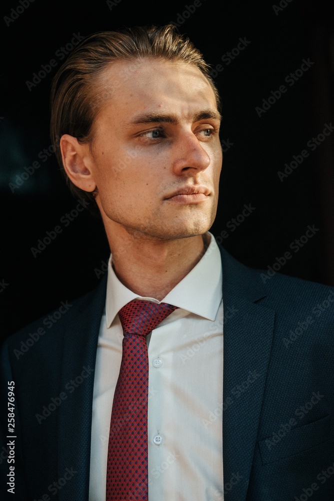 Male model in black suit and red tie poses for men's clothing advertising. Shooting for men's clothing store Male model in black suit and red tie poses for men's clothing advertising. Shooting for men's clothing store