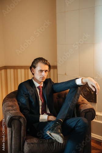 Male model in black suit and red tie poses for men's clothing advertising. Shooting for men's clothing store