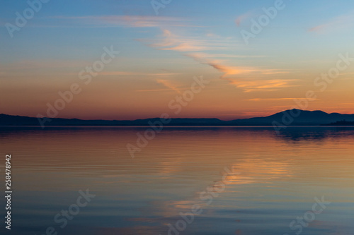 Symmetrcal, beautiful view of Trasimeno lake (Umbria, Italy) at sunset, with orange and blue tones in the sky
