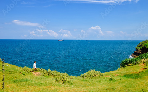 Chinese girl stands on grassland looking at ocean photo