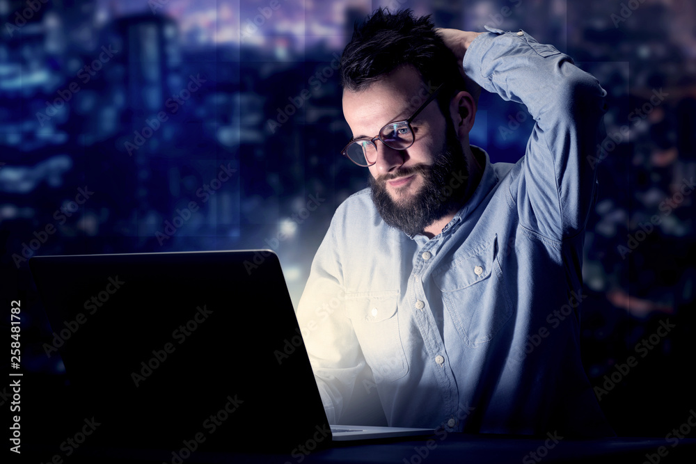 Young handsome businessman working late at night in the office with blue lights in the background Young handsome businessman working late at night in the office with blue lights in the background