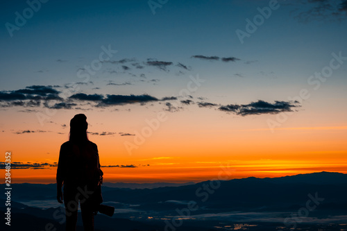 Back view of young hipster photographer holding the camera with sunset on mountain natural background.