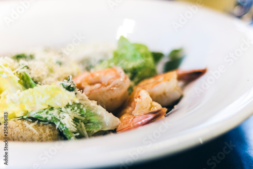 Caesar salad with shrimps on white plate in restaurant.