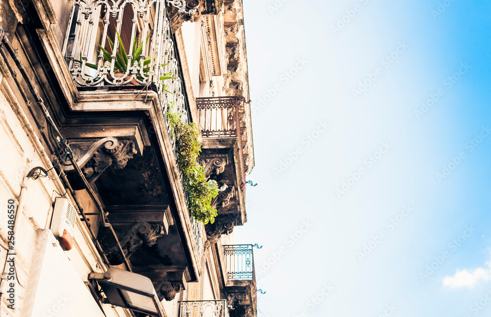 Balcony with flowerpots and house plants in a historic building in Catania, traditional architecture of Sicily, Italy.