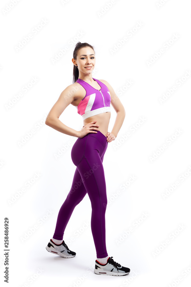 A dark-haired woman coach in a sporty pink short top and gym leggings posing, doing exercise, step forward on a white isolated background in studio A dark-haired woman coach in a sporty pink short top and gym leggings posing, doing exercise, step forward on a white isolated background in studio