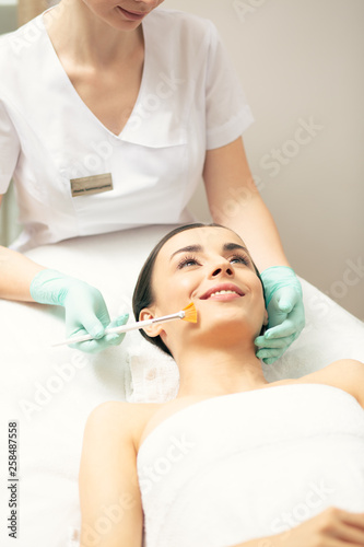 Smiling young woman enjoying peeling procedure in the clinic