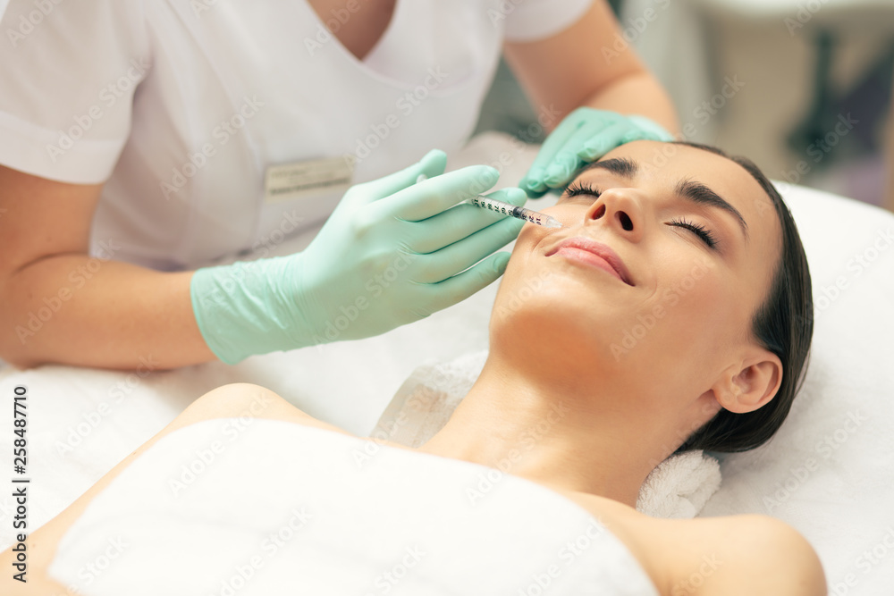 Relaxed woman having her eyes closed during the facial injections