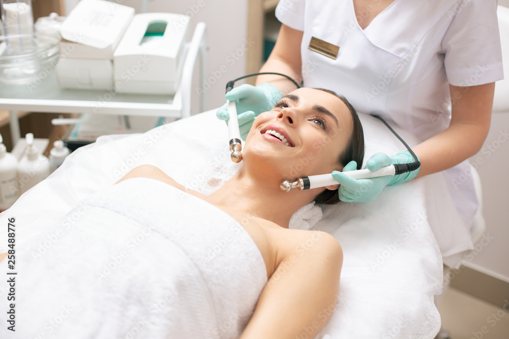 Excited woman lying in white towel during the microcurrent therapy