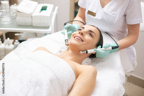 Excited woman lying in white towel during the microcurrent therapy