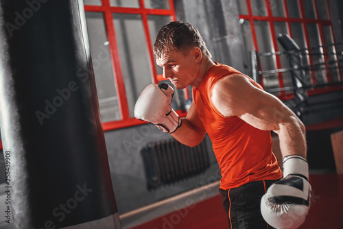 Stronger and faster. Handsome sportsman in sports clothing training on heavy punch bag in boxing gym